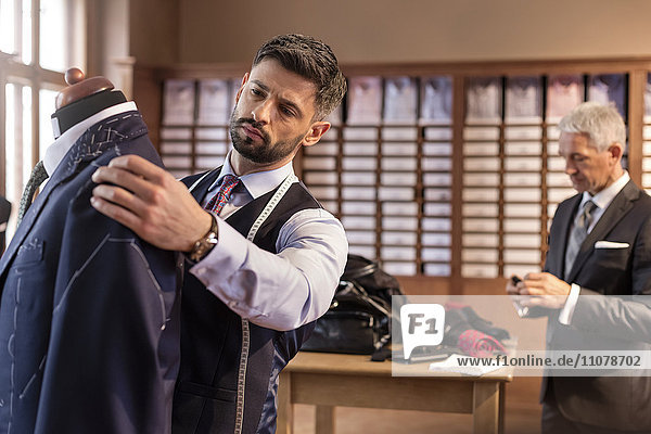 Tailor adjusting suit on dressmakers model in menswear shop