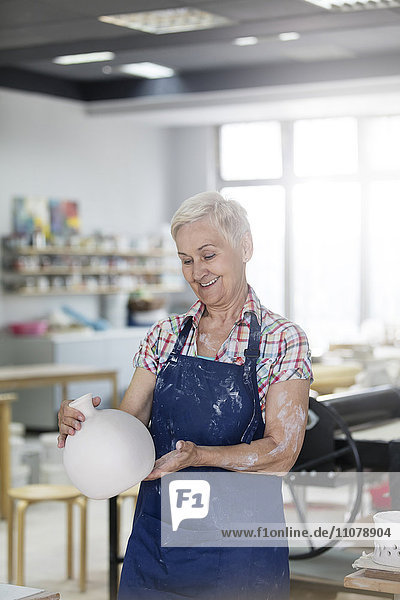 Lächelnde Seniorin mit Keramikvase im Atelier