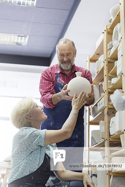 Lächelndes Paar stellt Keramikvase ins Regal im Atelier