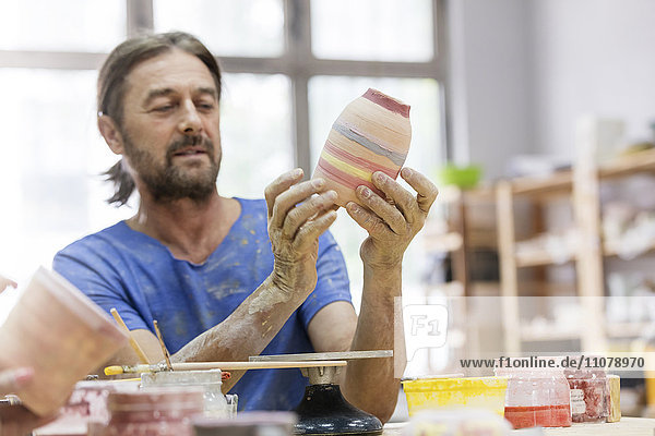 Reifer Mann malt Keramikvase im Atelier
