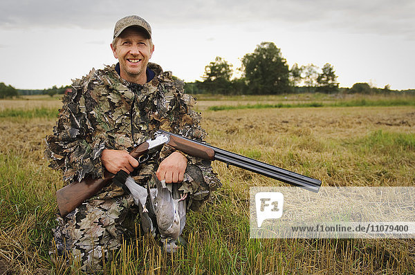 Hunter holding pigeon and rifle  smiling  portrait