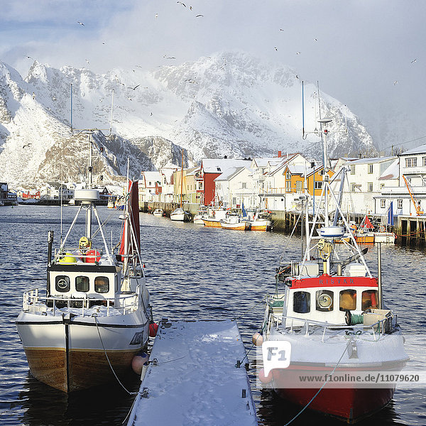 Fischerboote an der Anlegestelle  Dorf und schneebedeckte Berge im Hintergrund