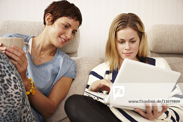 Two women sitting on sofa and using laptop