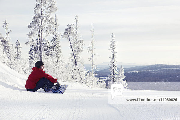 Woman with snowboard sitting and looking at view