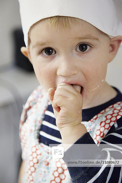 Junge mit Kochmütze und Finger im Mund