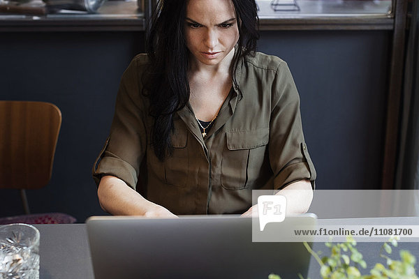 Großer Blickwinkel auf eine seriöse Geschäftsfrau  die mit dem Laptop am Tisch sitzt.