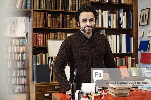 Portrait of smiling librarian standing against bookshelves