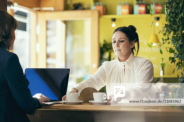Barista serviert Kaffee an Frau mit Laptop im Cafe