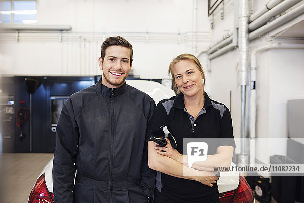 Portrait of happy mechanic standing with female in auto repair shop