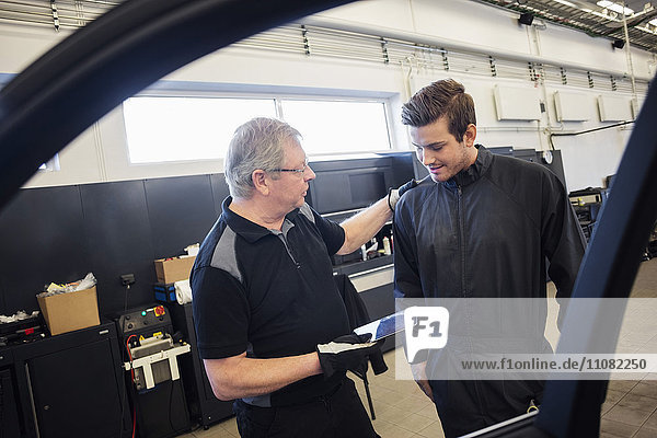 Mechanics using digital tablet seen through car window at auto repair shop