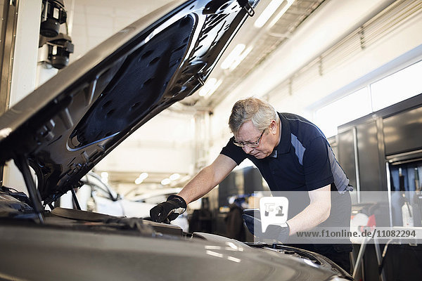 Senior Mechaniker hält Handy während der Reparatur des Autos in der Werkstatt