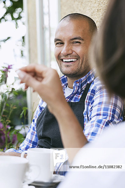 Lächelnder Mann mit Mitarbeiterin sitzt am Tisch vor dem Café