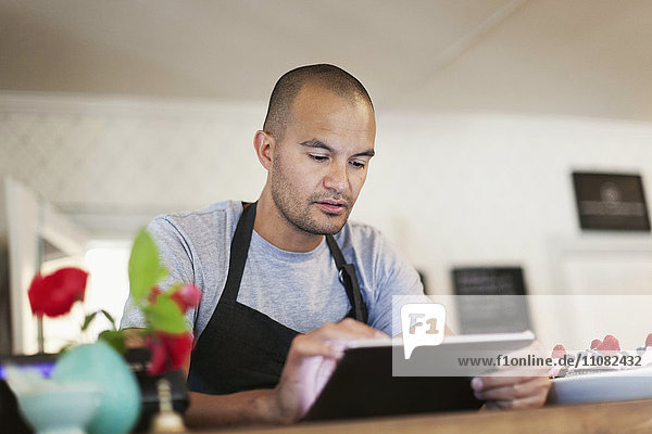 Männlicher Besitzer mit digitalem Tablett am Cafe-Schalter