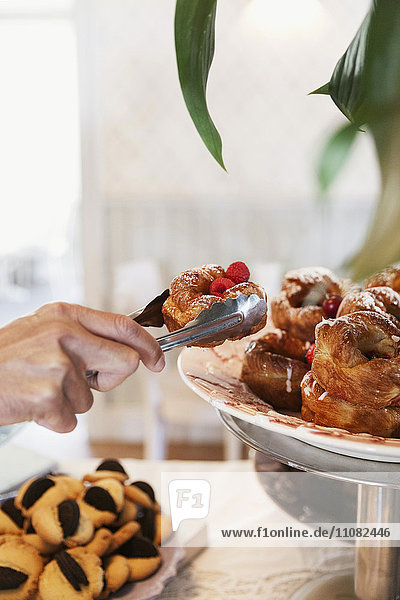 Abgeschnittenes Bild von Hand hält Dessert mit Zange von cakstand im Cafe