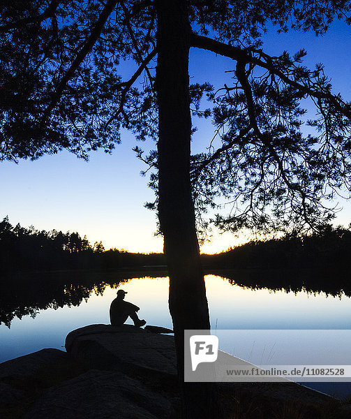 Sitzender Mann mit Blick auf den See in der Abenddämmerung
