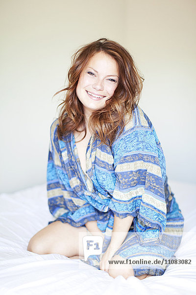 Lächelnde junge Frau auf dem Bett im Bademantel