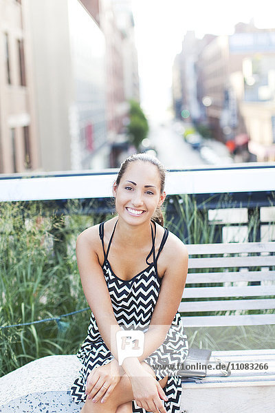 Lächelnde junge Frau auf einer Bank sitzend  New York City  USA