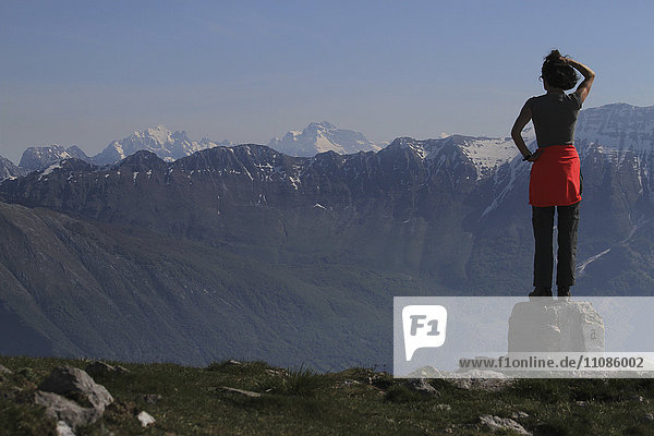 Rückansicht einer Frau  die auf einem Felsen gegen die Berge steht.