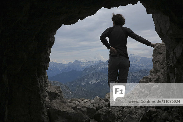 Rückansicht der Frau  die auf einem Felsen gegen die Berge steht  durch die Höhle gesehen.