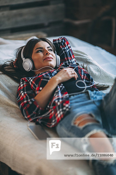 Trendige junge Frau  die zu Hause auf dem Bett liegt und Musik hört.