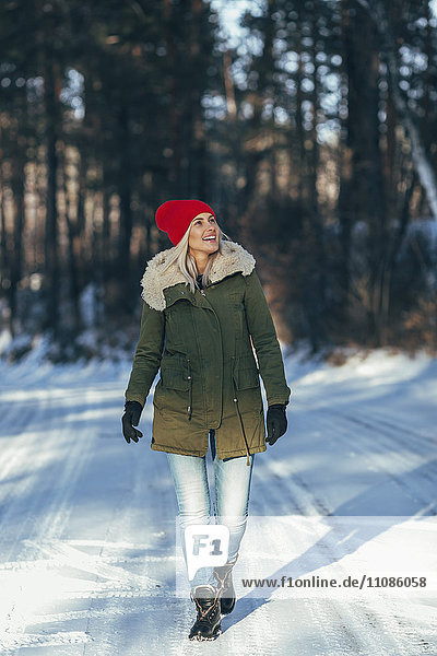 Volle Länge der glücklichen Frau  die auf schneebedecktem Feld läuft.