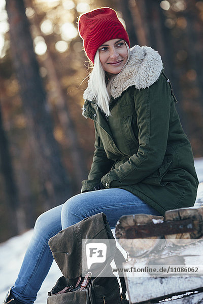 Young woman looking away while sitting on log during winter