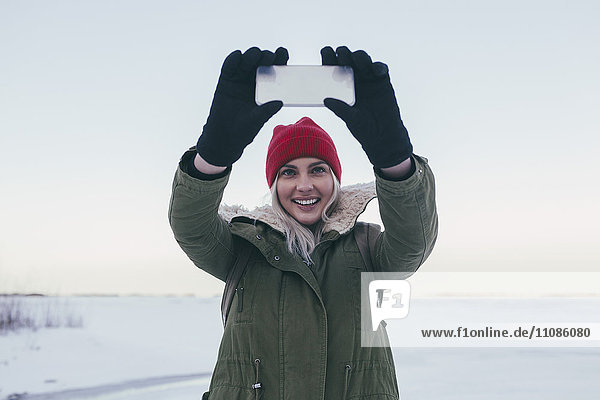 Junge Frau nimmt Selfie auf Smartphone im Winter