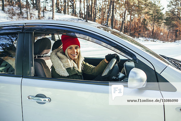 Porträt einer lächelnden Frau in warmer Kleidung beim Autofahren