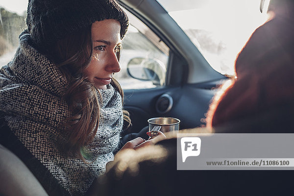 Junge Frau mit Kaffeetasse und Blick auf den Mann im Auto
