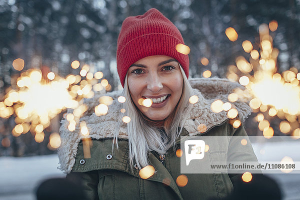 Porträt einer lächelnden Frau  die im Winter Wunderkerzen hält.