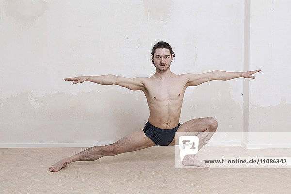 Porträt eines entschlossenen Mannes  der Yoga in Kriegerposition vor weißem Hintergrund praktiziert.