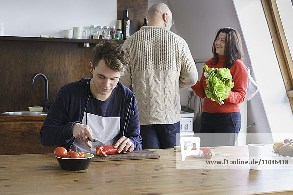 Teenager schneiden Gemüse auf dem Tisch und helfen Eltern in der Küche