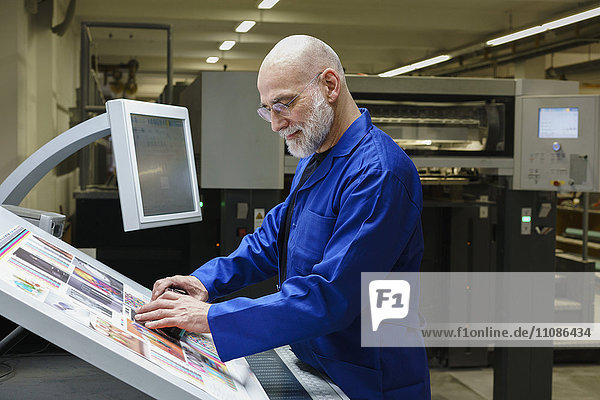 Ausgereifter Mann bei der Qualitätskontrolle des Ausdrucks mit Scanner an der Druckmaschine