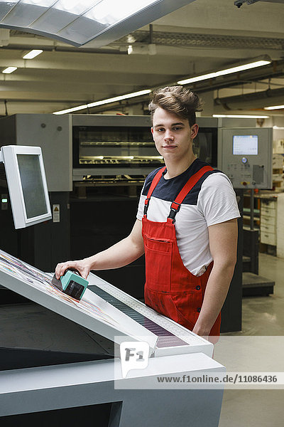 Portrait eines jungen Arbeiters  der den Scanner über den Ausdruck mit Maschinen an der Druckmaschine hält.