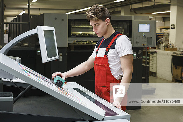 Young worker doing quality check of printout with machinery at printing press