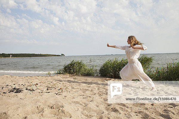 Young woman practicing yoga on sea shore at beach against sky