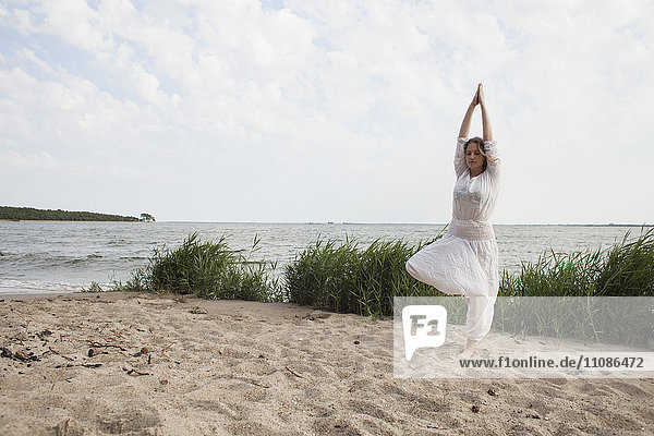Young woman practicing yoga on sea shore against sky