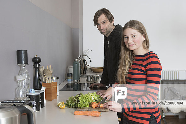 Portrait of father and daughter chopping vegetables at kitchen counter