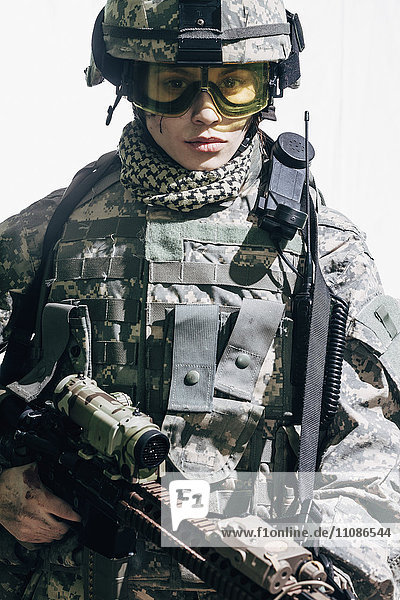 Portrait of female soldier carrying rifle and standing against white background