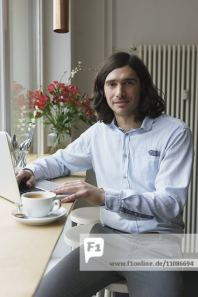 Porträt eines Mannes mit Laptop beim Kaffeetrinken im Cafe