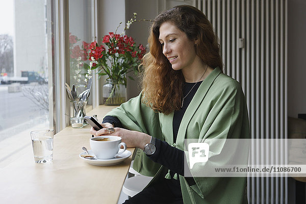 Young woman using phone and having coffee at cafe
