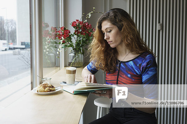 Young woman reading book while having breakfast at cafe