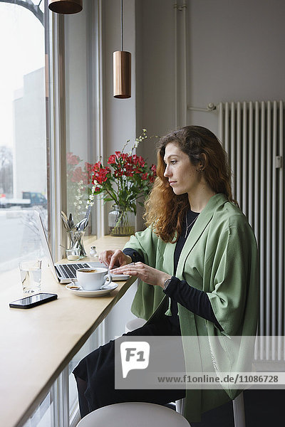 Nachdenkliche Frau mit Laptop beim Kaffeetrinken im Cafe