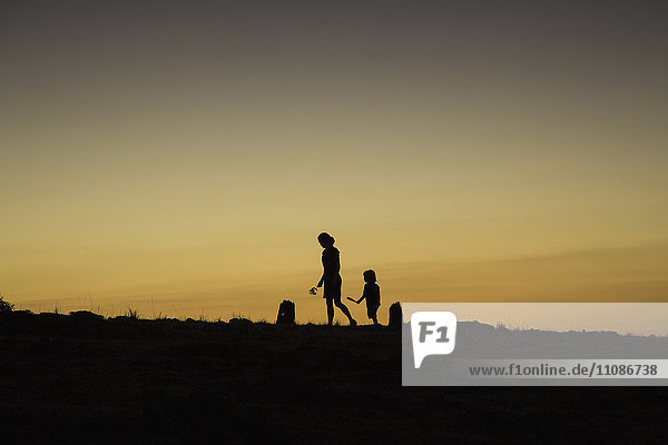 Silhouette woman and boy walking on field against clear sky during sunset
