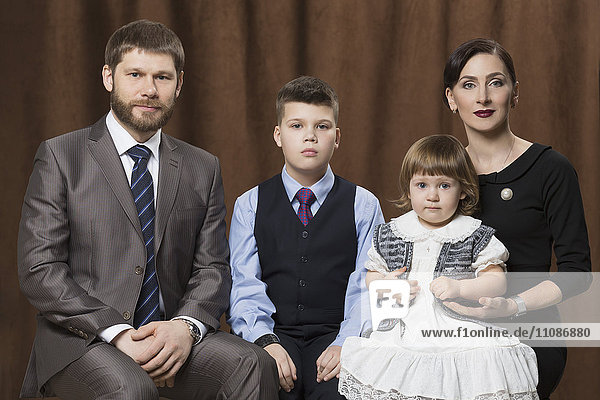 Porträt einer Familie  die gegen braune Vorhänge im Atelier sitzt.