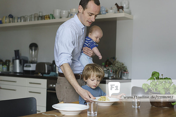 Father carrying toddler while giving food to son at dining table