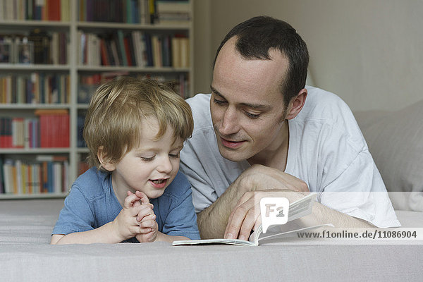Father and son reading book while lying on bed at home