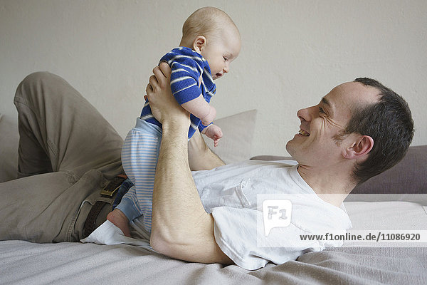 Lächelnder Vater hält den Sohn und liegt zu Hause im Bett.