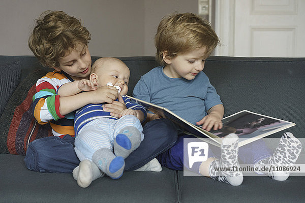 Junge liest Buch  während er neben seinen Brüdern zu Hause sitzt.