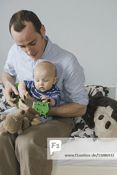 Kleinkind schaut Vater beim Spielen von Spielzeuggitarre zu Hause an